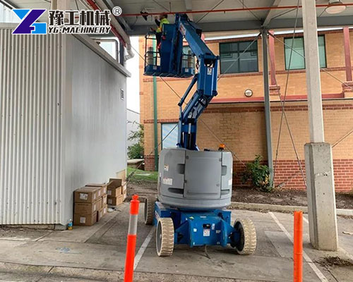 Electric Knuckle Boom Lift operating indoors near pallet racks